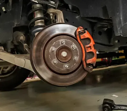 Ford brake rotor and orange caliper exposed during brake repair