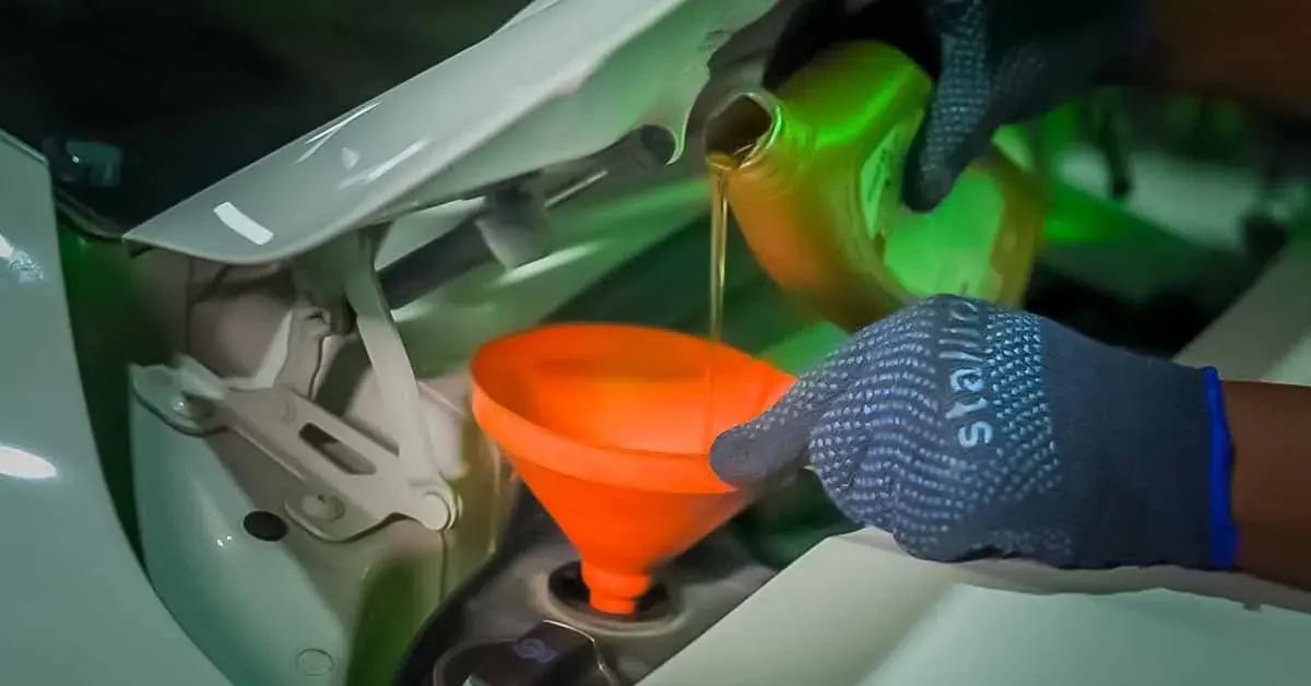 Technician pouring synthetic engine oil through a funnel